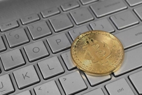 Dizüstü bilgisayar klavyesi üzerinde duran Bitcoin temsili madeni para